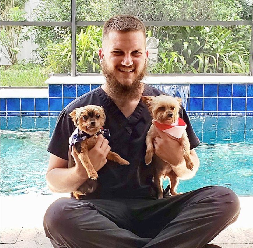 Groomer sitting by a Tampa lanai pool holding two small freshly groomed dogs in bandanas